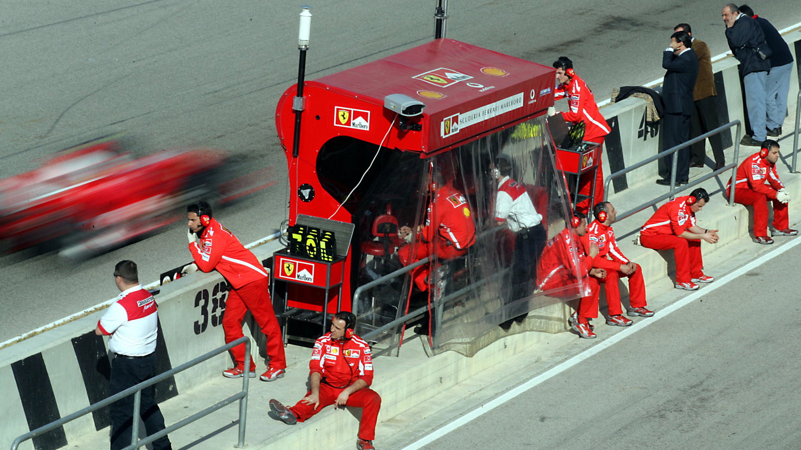 The Ferrari team relax on the pit wall as Rubens Barrichello drives past